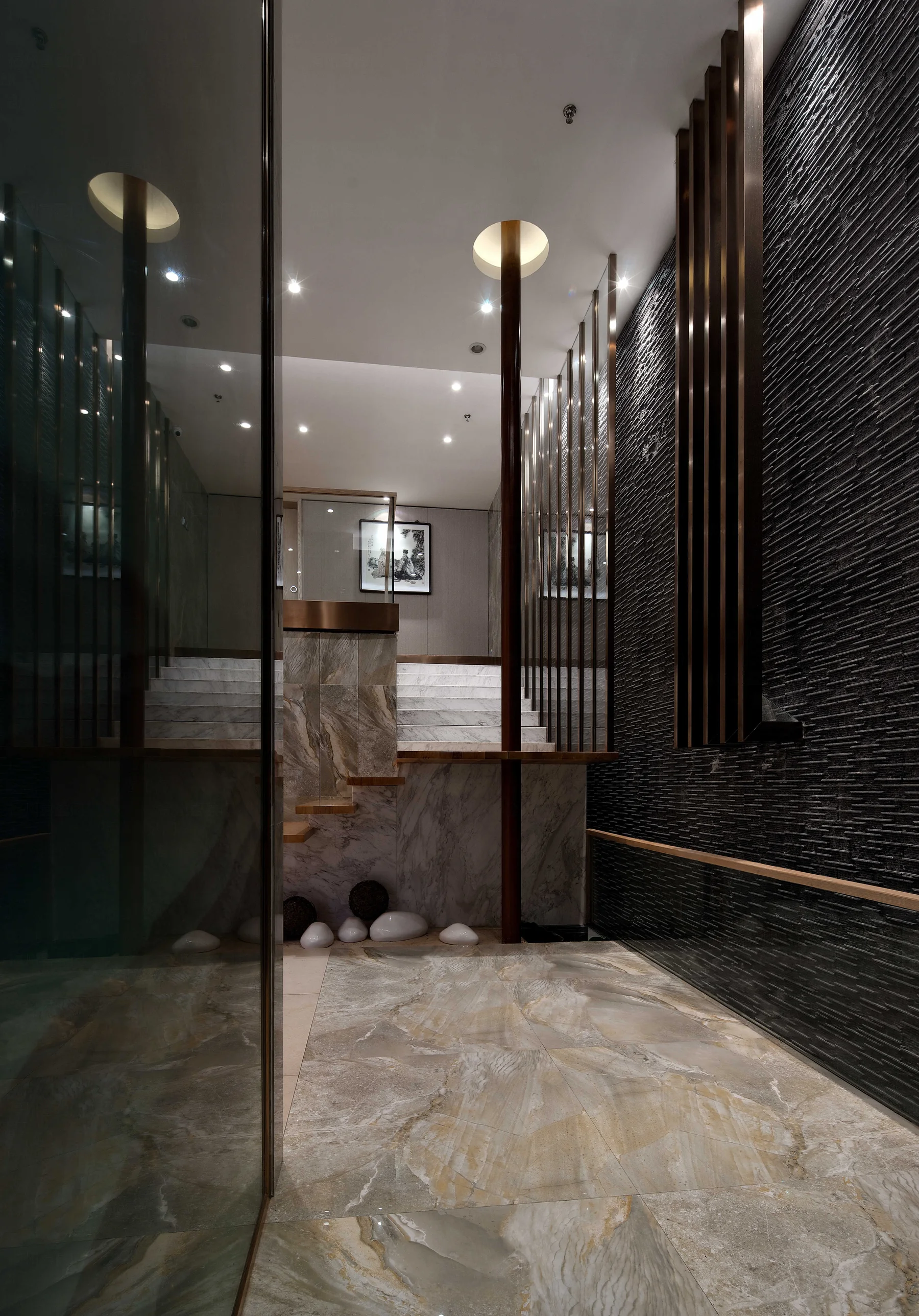 Reflective corridor framed by dark stone and slender bronze posts