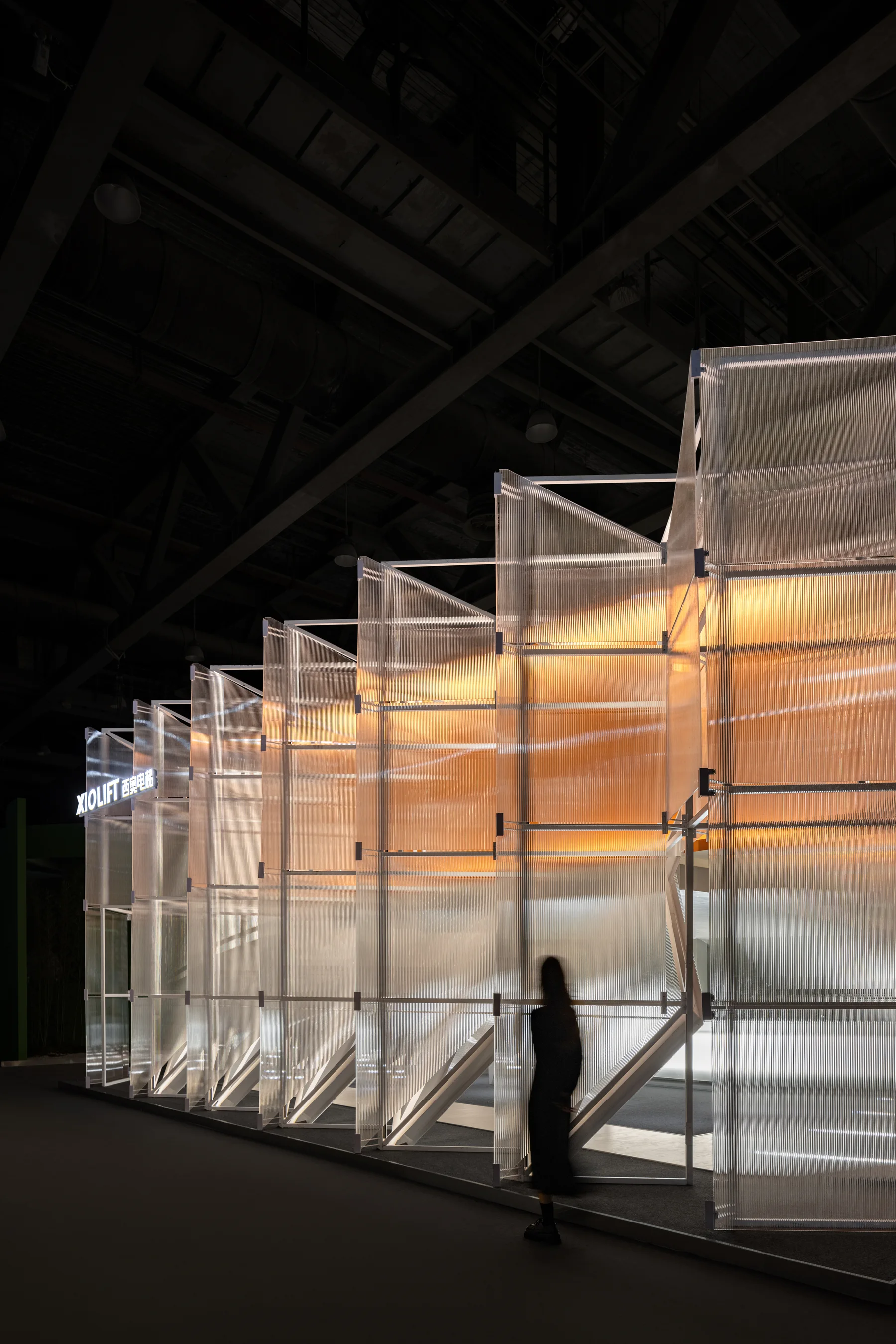 A translucent modular display structure with exposed metal braces and panel connections at the XioLift Floating Cube Showroom.